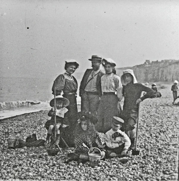 Deux femmes, un homme au canotier et quatre enfants avec seaux et pelles sur une plage de galets